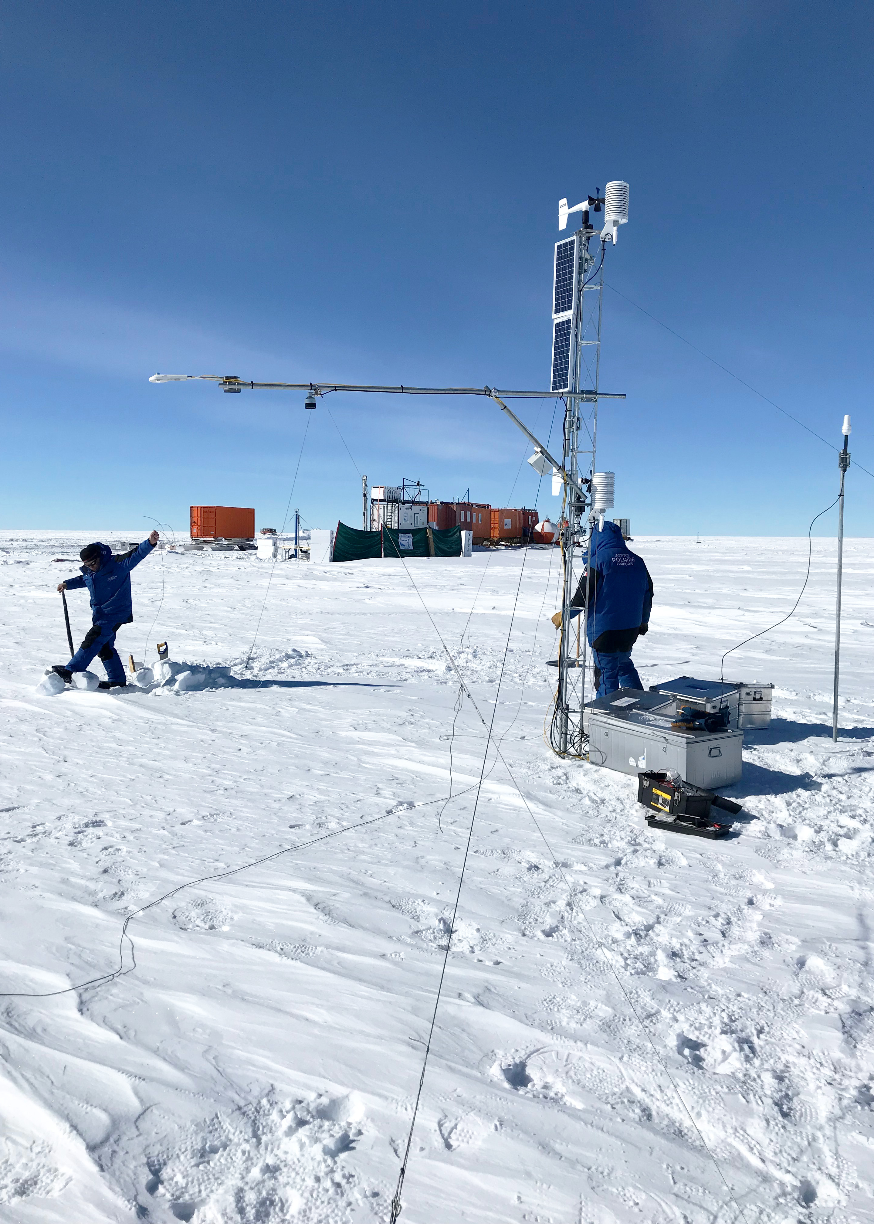 <p>Installation d'une station météo automatique fonctionnant sur panneaux solaires et batteries. Les données sont collectées en continu par transmission satellite. En arrière plan, le site de forage protégé du vent par des bâches et une partie du convoi EAIIST (Laboratoire et caravanes vie et énergie)<br class='autobr' />
© J Savarino, CNRS/IPEV/PNRA</p>